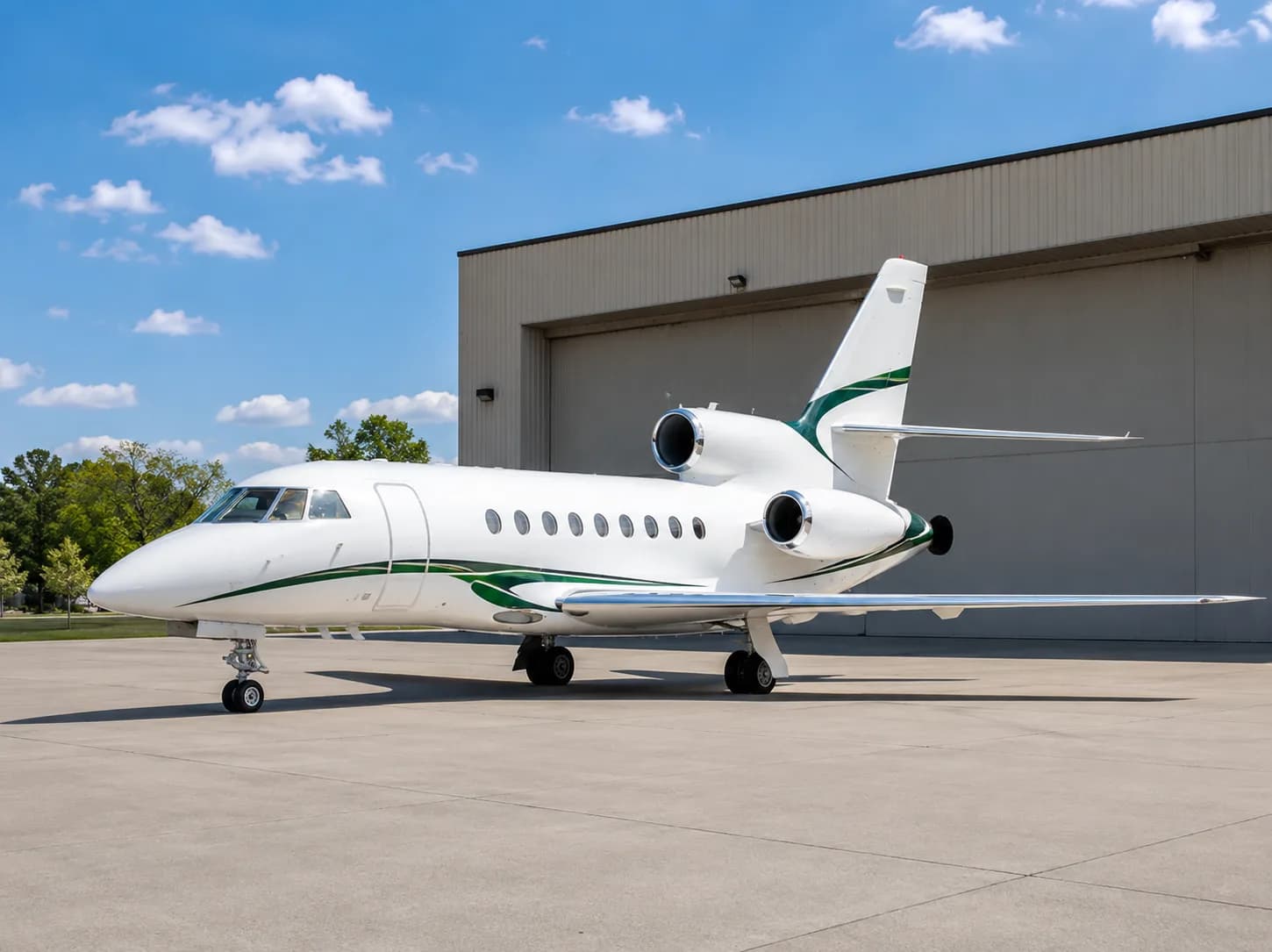 A white business jet with green stripes on the fuselage and tail, parked on a tarmac in front of a hangar under a blue sky.