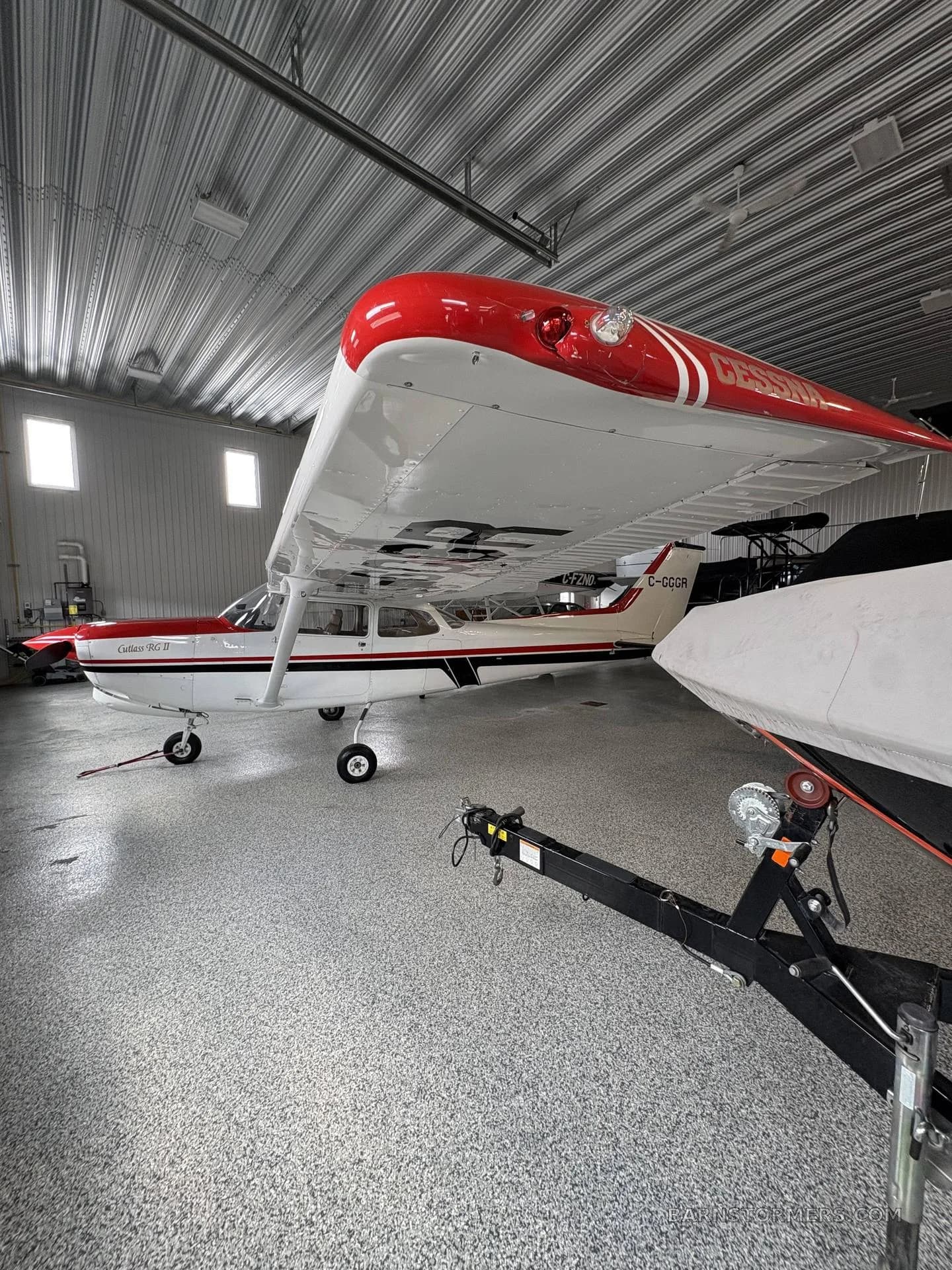 A white and red Cessna Cutlass RG II (C-GGCR) parked in a hangar, viewed from the front right.