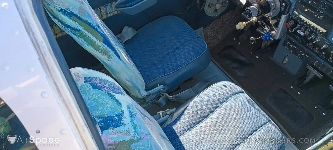 The interior cabin of a light aircraft, showing blue fabric seats and part of the cockpit controls.
