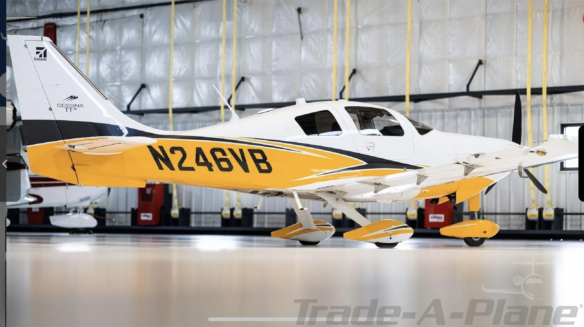 A side view of the white and yellow Cessna TTx aircraft N246VB parked in a hangar.
