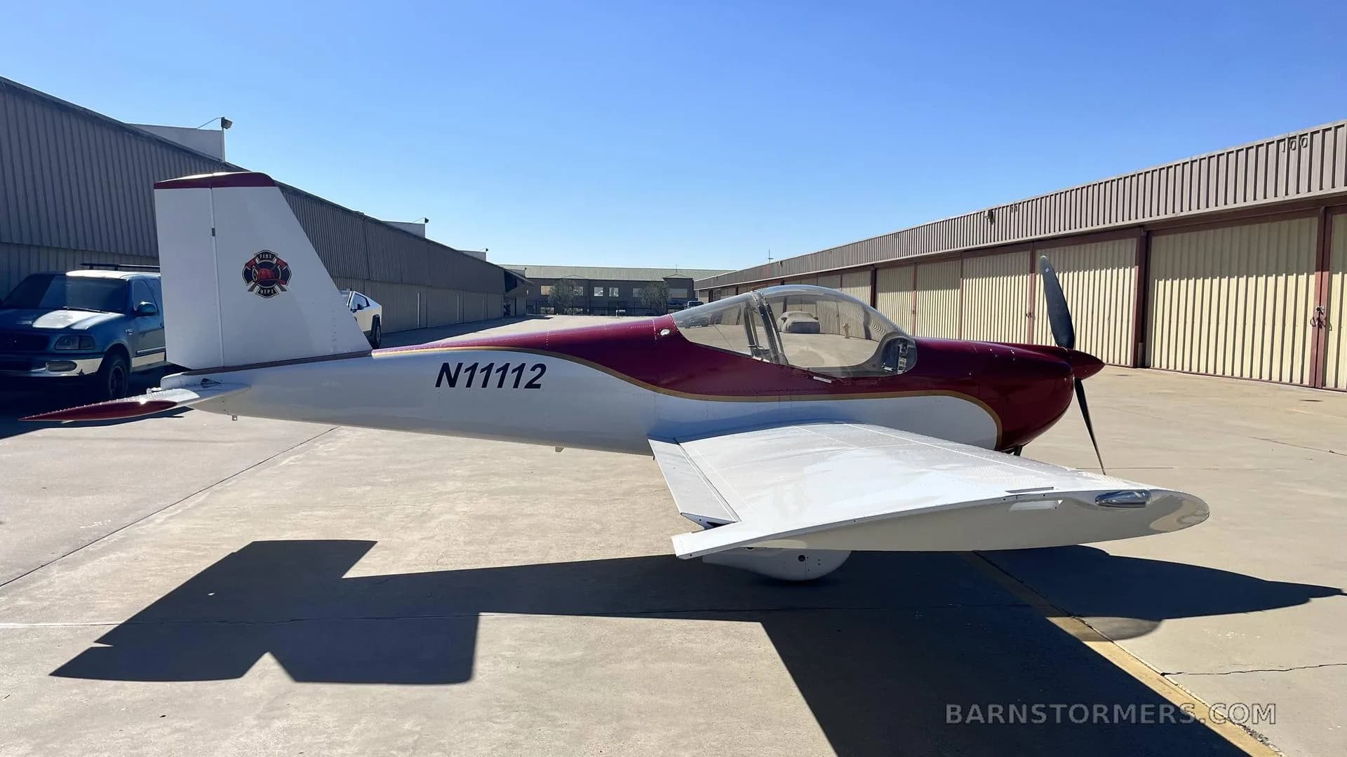 A red and white single-engine aircraft with registration N11112 is parked on an airfield apron, viewed from the right side.
