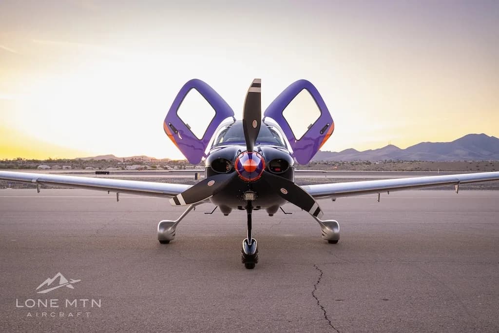 Front view of a purple and silver Cirrus SR22T with open doors, parked on a tarmac at sunset.