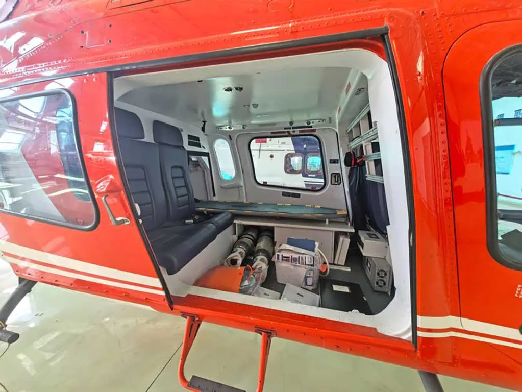 The open side door of a red and white helicopter, revealing the cabin interior with blue seats and equipment.