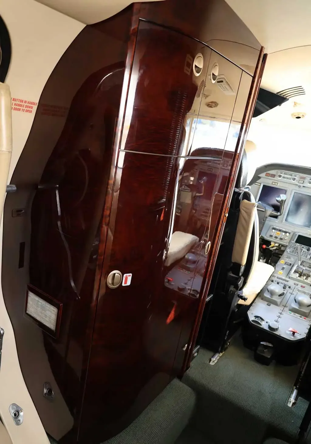 A dark wood cabinet with a glossy finish inside the private jet cabin, with a glimpse of the cockpit instruments.