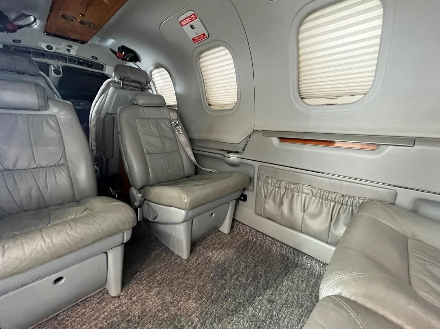 The aircraft cabin interior featuring multiple rows of light gray leather seats and window shades.