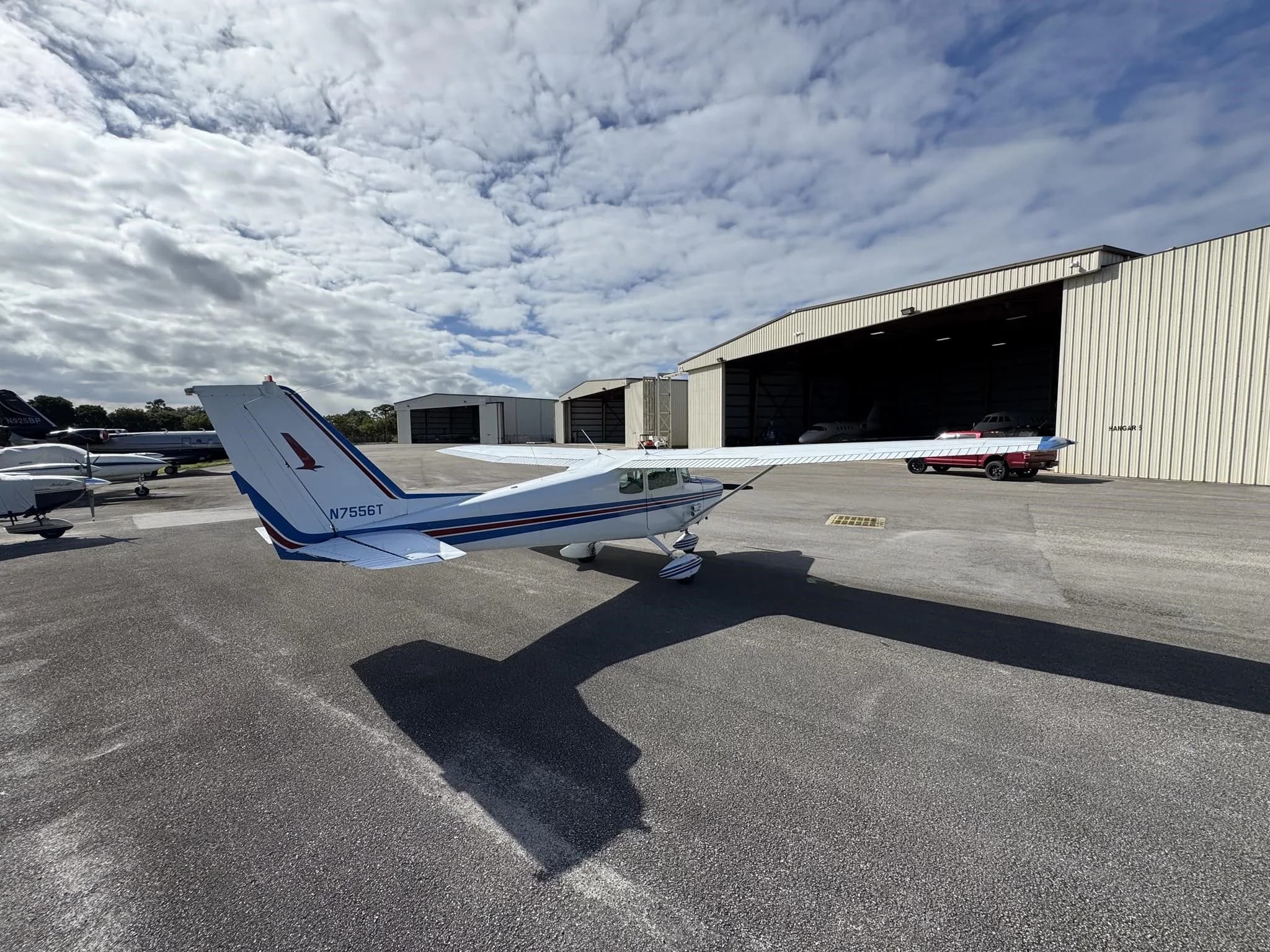 A white and blue Cessna 172 (N7556T) parked on an airfield, showing the tail and right wing.