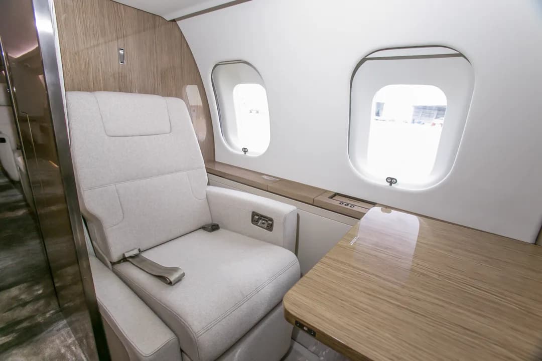 A single light-colored fabric seat with a wooden side table next to two aircraft windows.