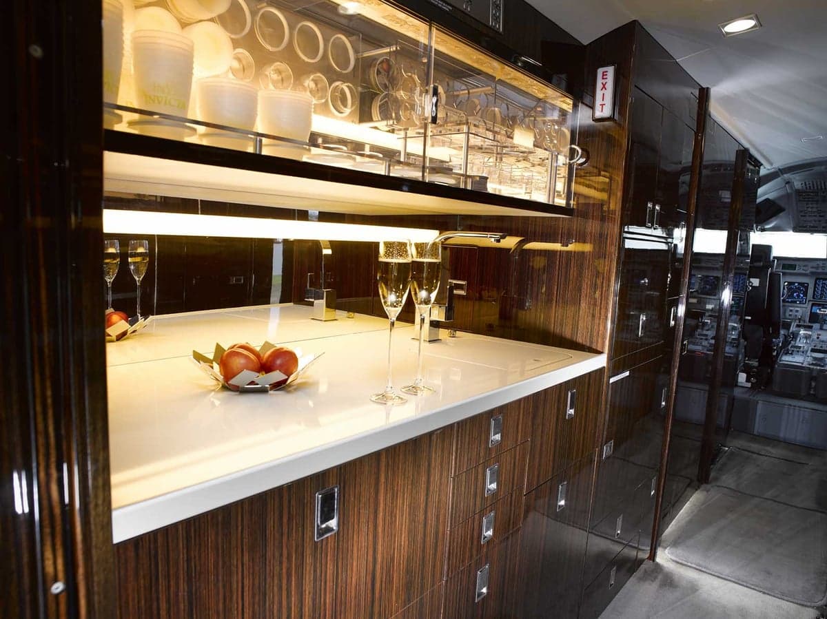 The galley area of the Gulfstream G650 cabin, featuring a counter with champagne glasses and a display cabinet.