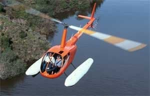 Orange Robinson helicopter with floats flying over water.