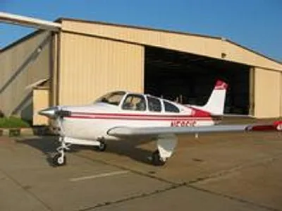 A white and red Beechcraft Bonanza N5861S parked on an asphalt ramp in front of an open hangar.