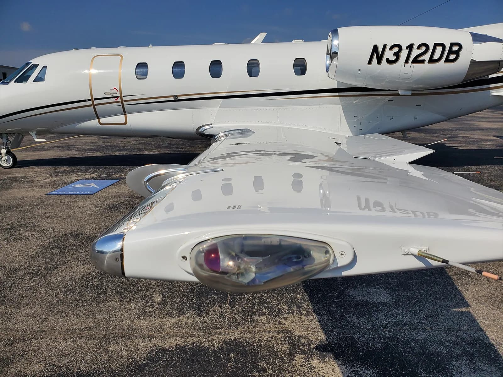 A close-up view of the right wing and fuselage of a white private jet with gold and black stripes, showing the wingtip light and engine.