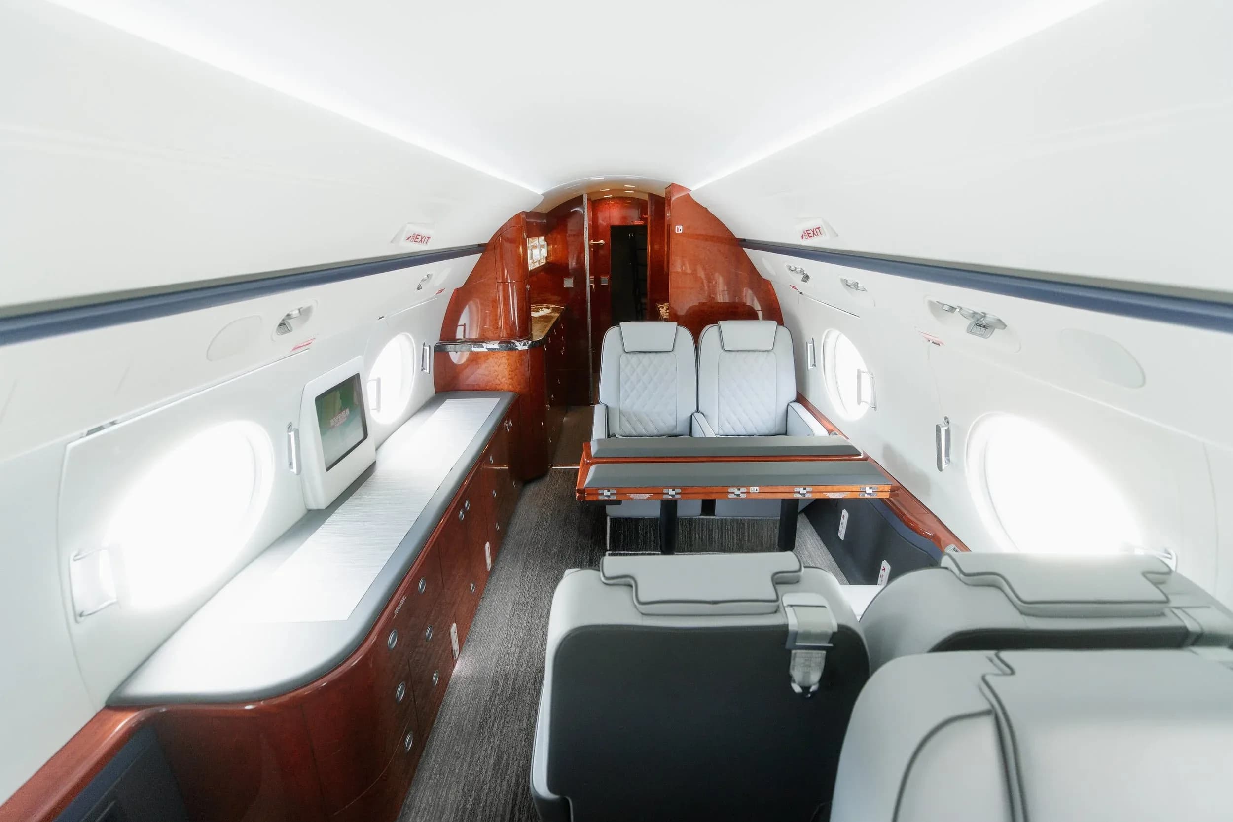 The rear section of the private jet's cabin, featuring a dining table setup and a long side couch, with rich wood paneling.