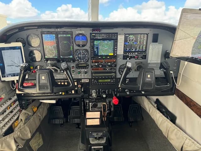 A full view of the modern glass cockpit of a Cessna 206, featuring multiple digital displays and traditional controls, with N7567K visible.