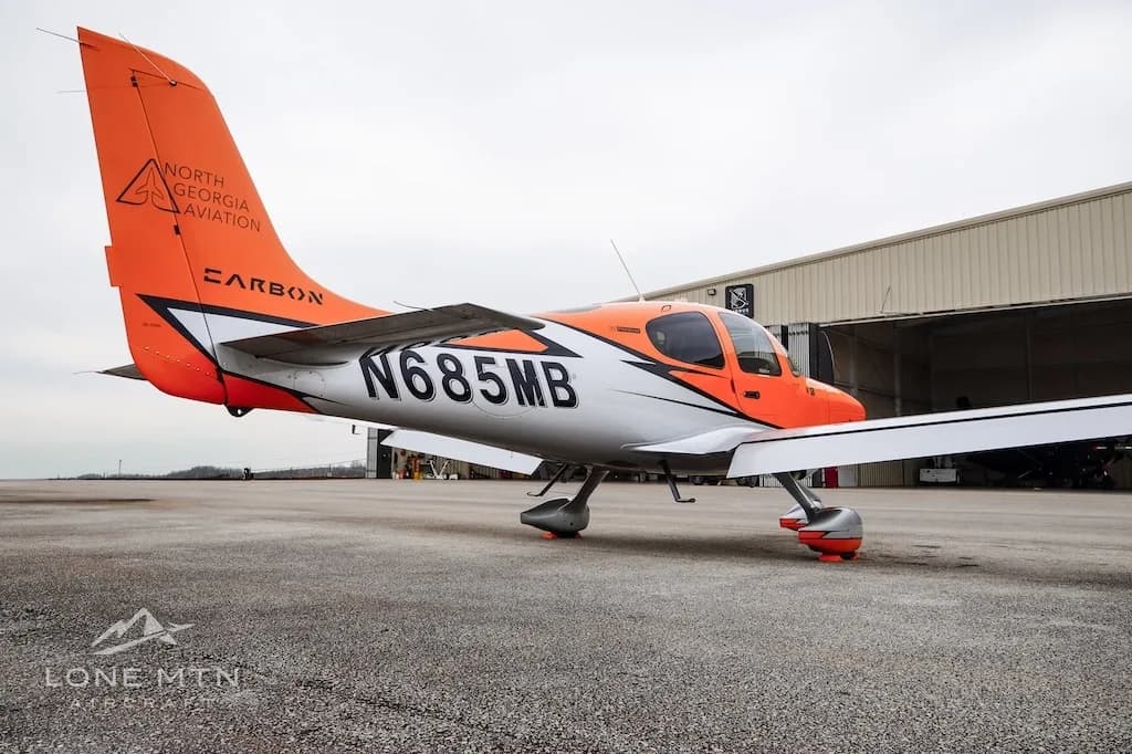 A low-angle side view of the orange and silver Cirrus SR20 aircraft N685MB on an airfield.