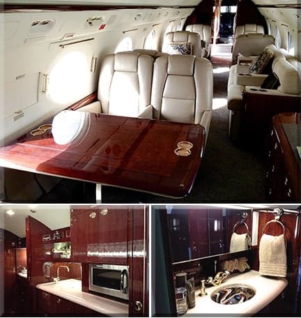 Interior of the aircraft featuring leather seats, a wooden table, and a kitchenette and bathroom area.