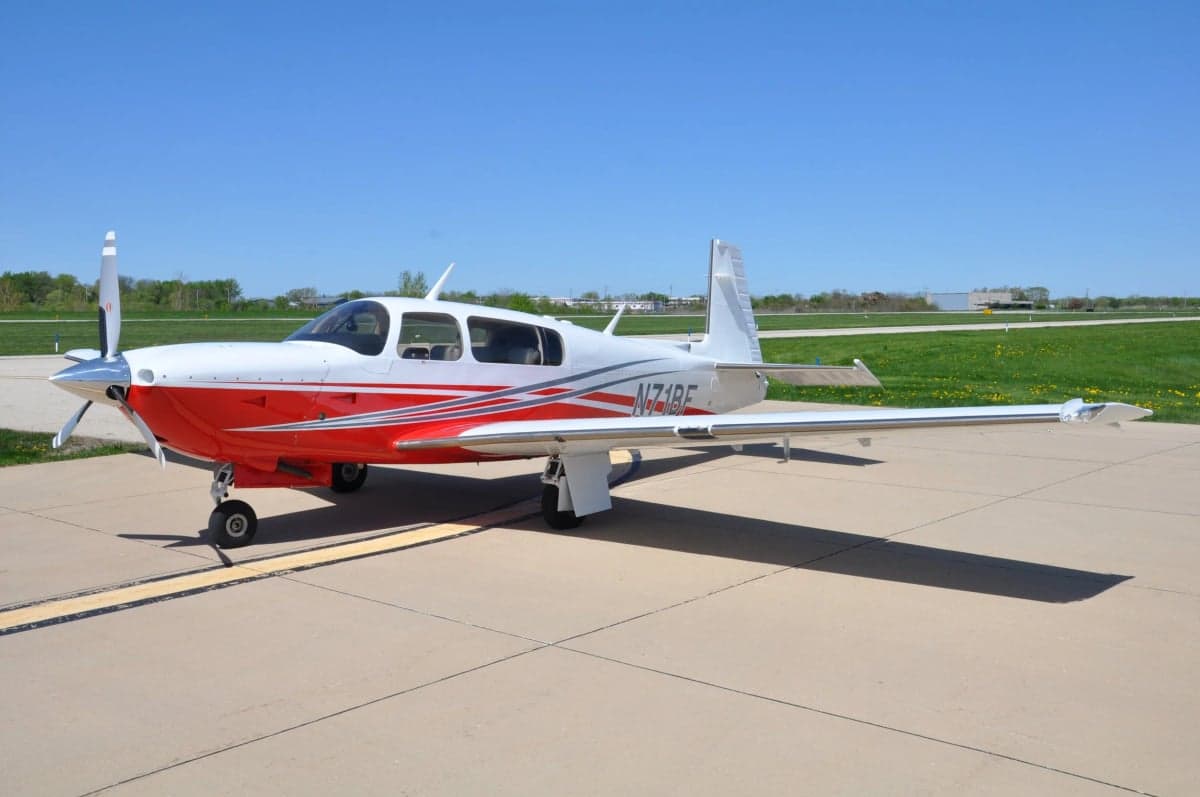 A Mooney M20J aircraft with a white and red paint scheme parked on the tarmac.