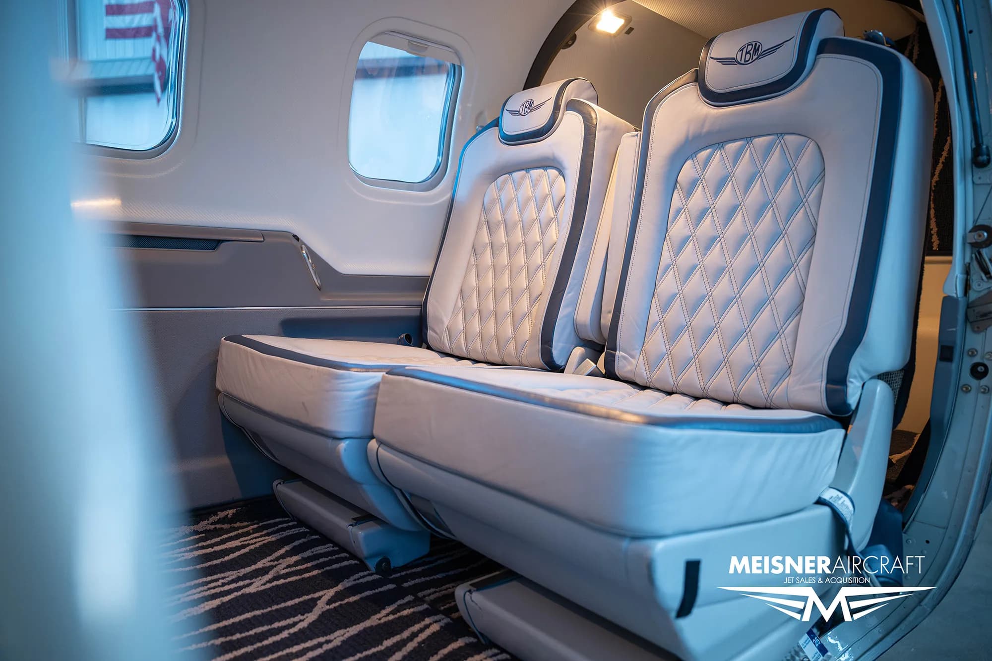 A view of two quilted leather aircraft cabin seats with the TBM logo on the headrests, seen from a slightly different angle.