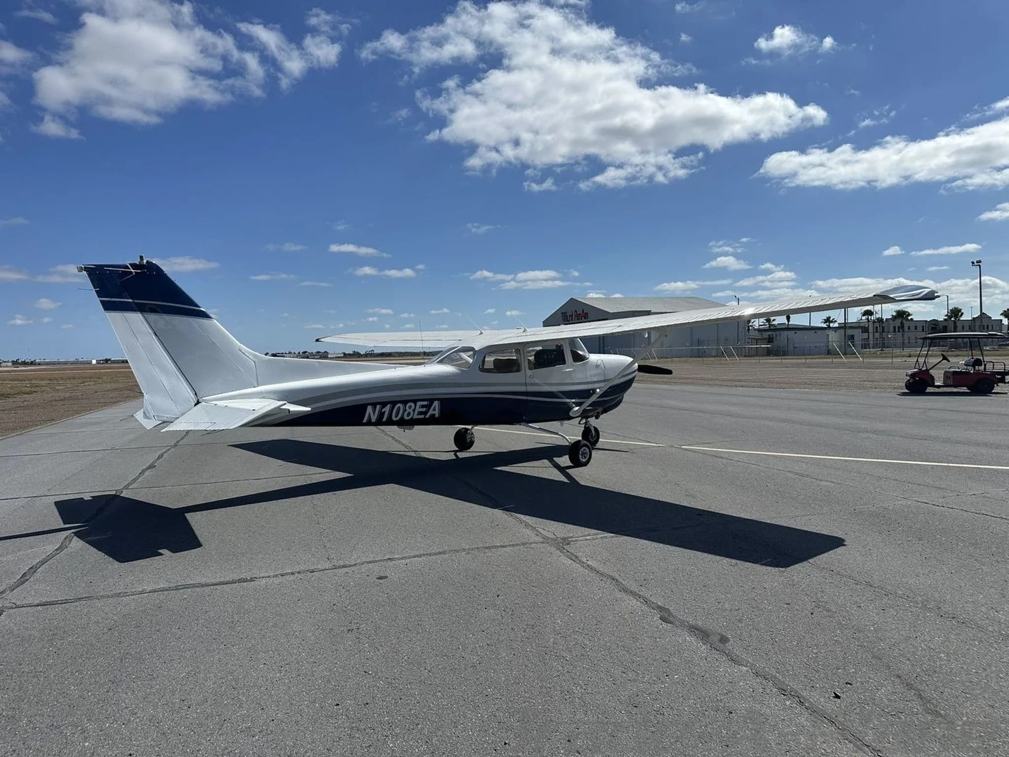 Rear three-quarter view of a white and dark blue Cessna N108EA aircraft on an airport tarmac.