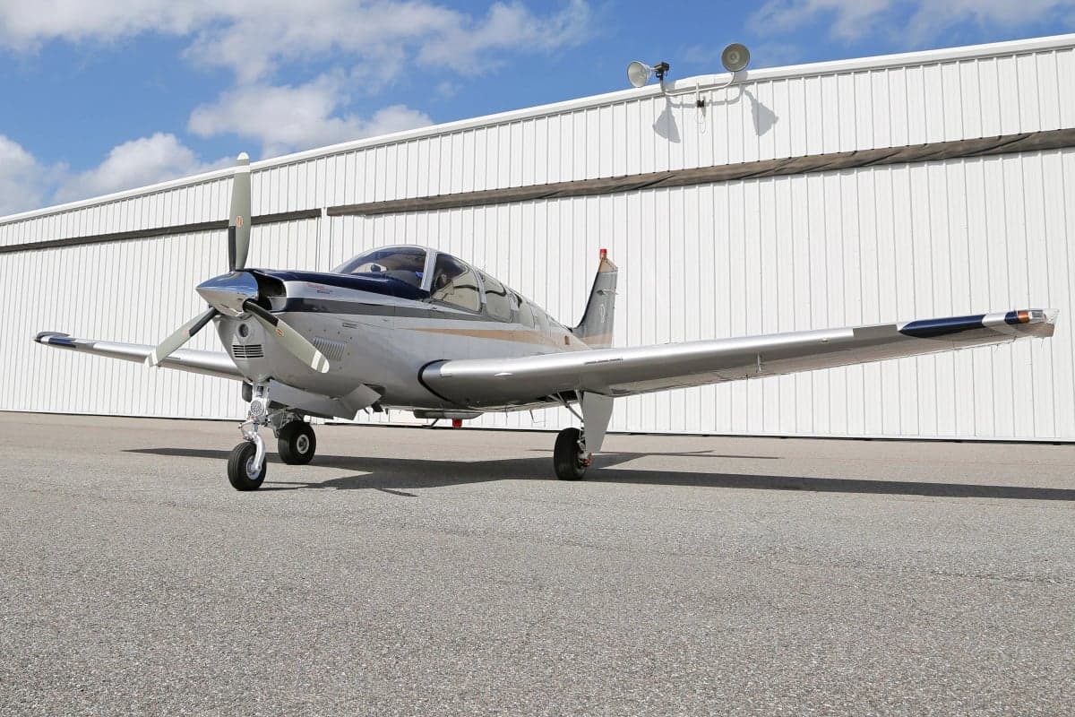 A Beechcraft Bonanza aircraft parked on the tarmac in front of a hangar.