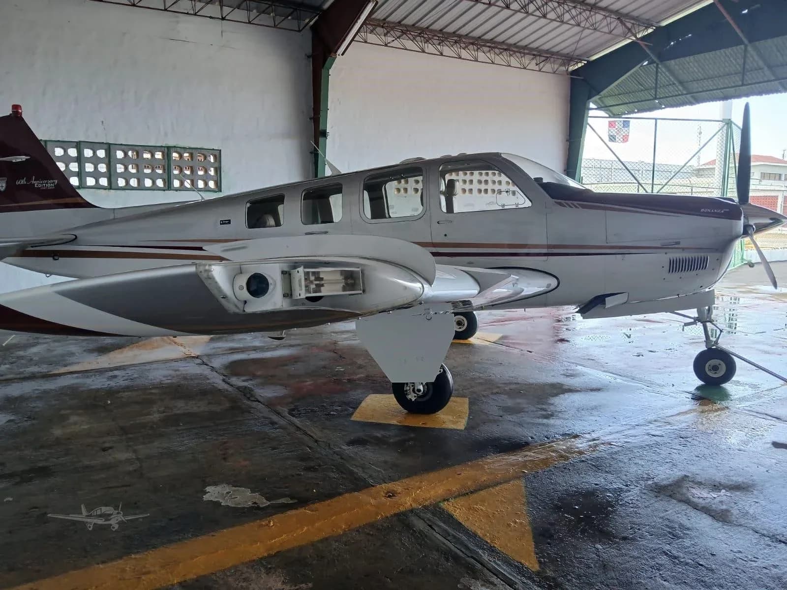 A Beechcraft Bonanza with a silver and maroon paint scheme parked in a hangar.