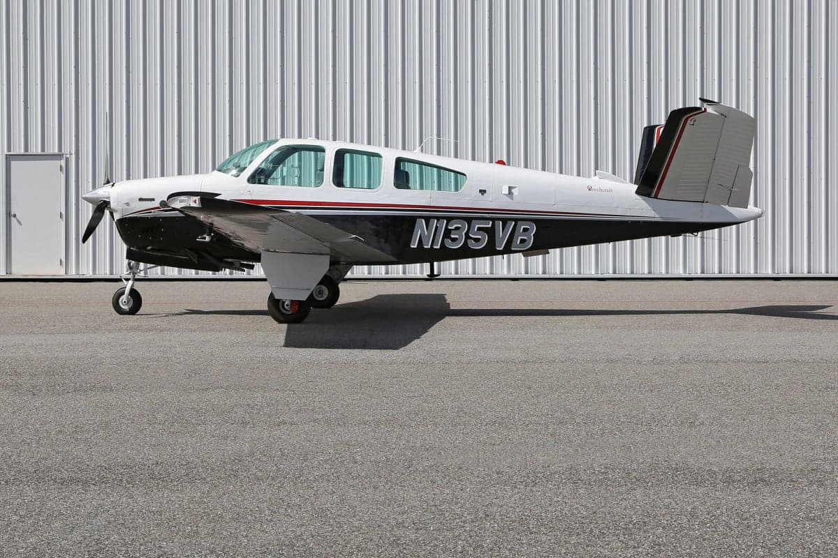 Side view of a Beechcraft Bonanza aircraft on the ground in front of a hangar, showing the tail number N135VB.
