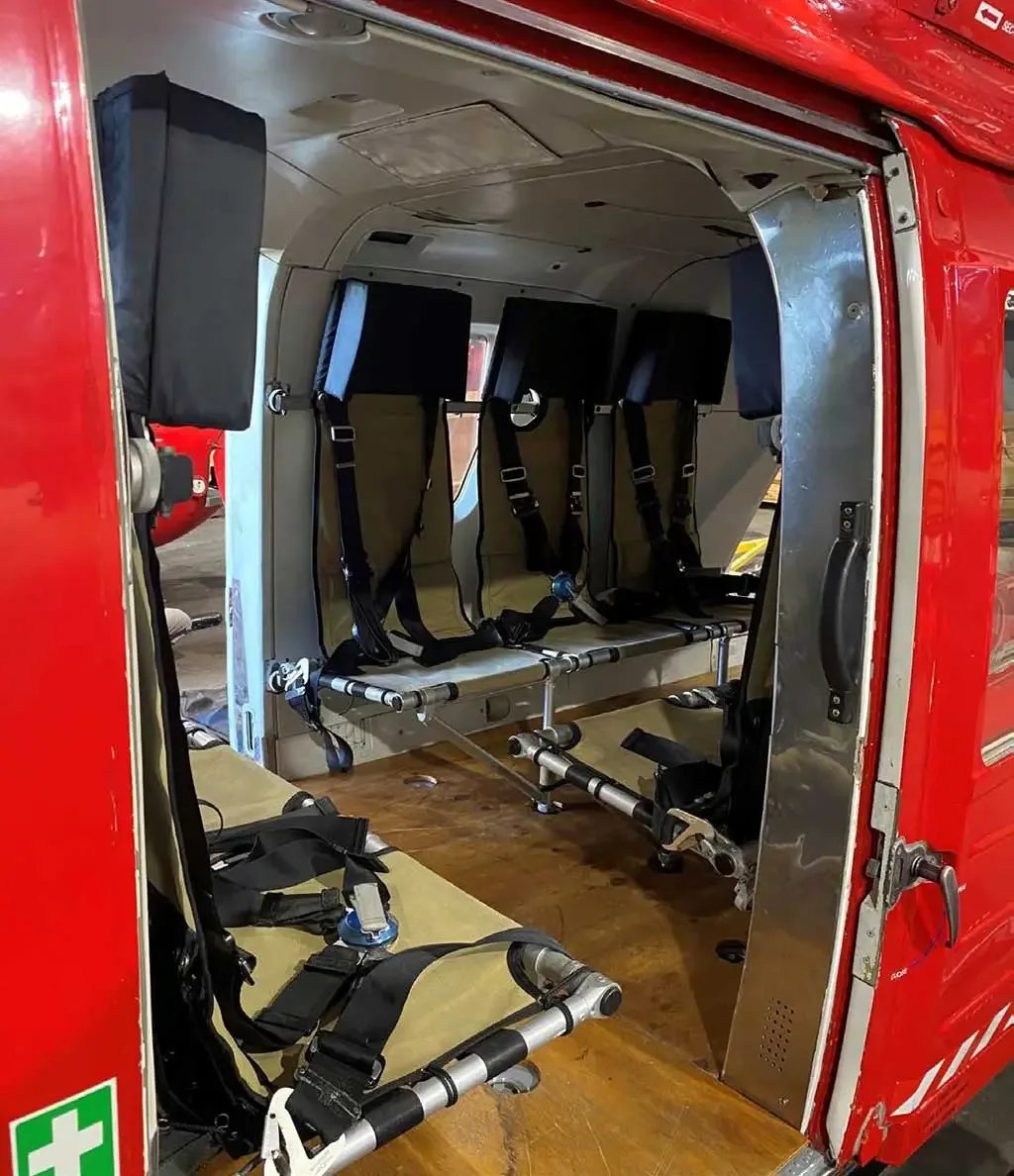 The open side door of a red helicopter revealing the interior cabin with tan fabric seats.