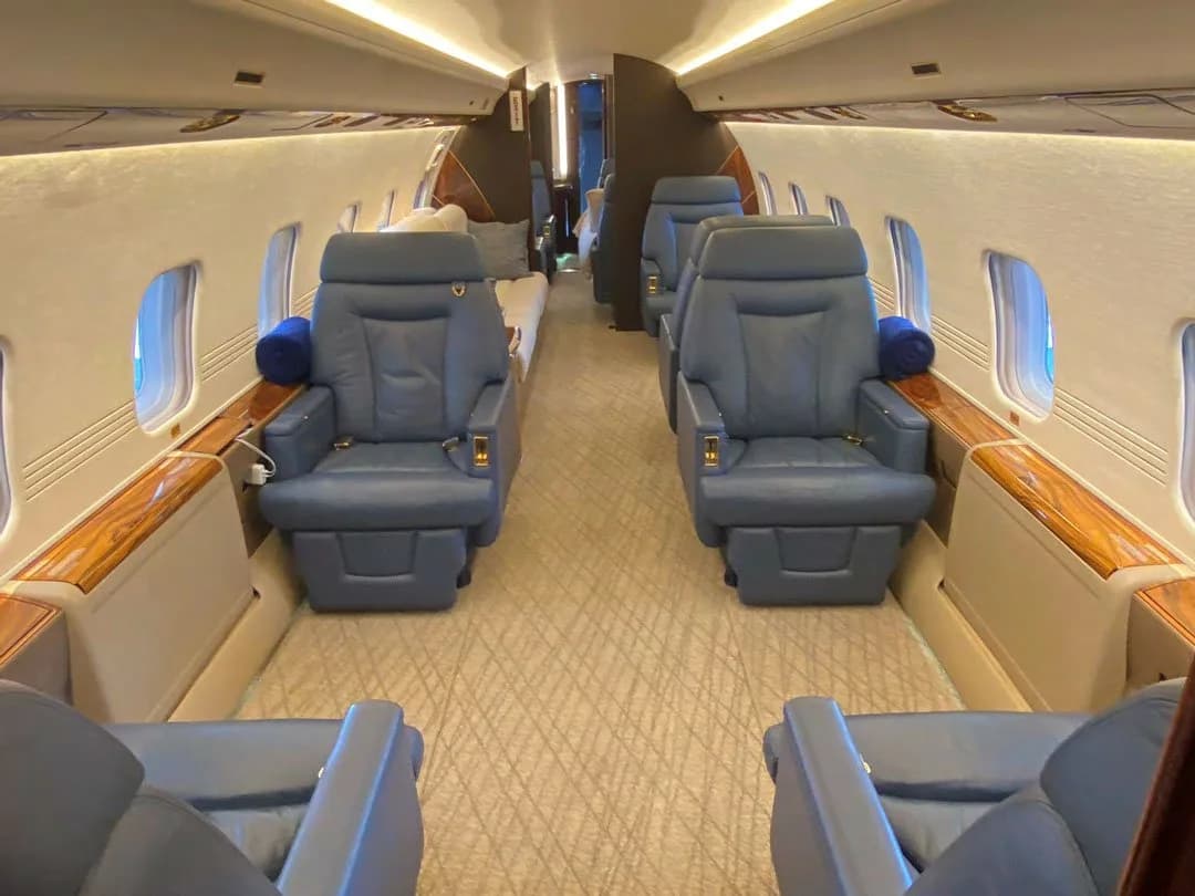The spacious cabin interior of a business jet features multiple rows of blue leather seats and a patterned carpet.