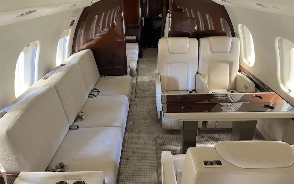 The spacious interior of a private jet featuring a cream sofa, individual seats, and a dining table.