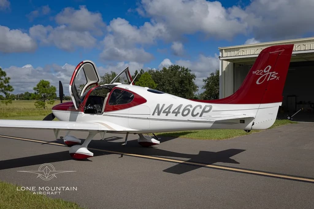 A red and white Cirrus SR22 aircraft (N446CP) with its doors open, viewed from the rear-right, parked on an asphalt ramp.