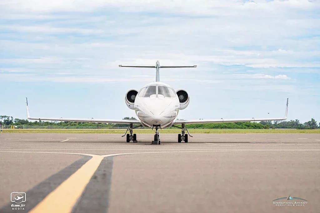 A head-on view of a white business jet with blue stripes, tail number N558RJ, parked on an airfield.