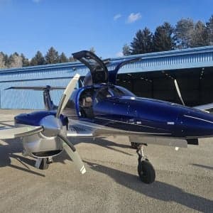 A blue and silver Diamond DA62 aircraft is parked on the tarmac with its gull-wing doors open.