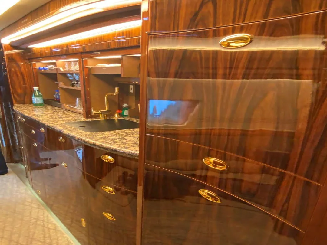 A close-up of the aircraft galley shows polished dark wood cabinets with gold handles, a sink, and a granite countertop.