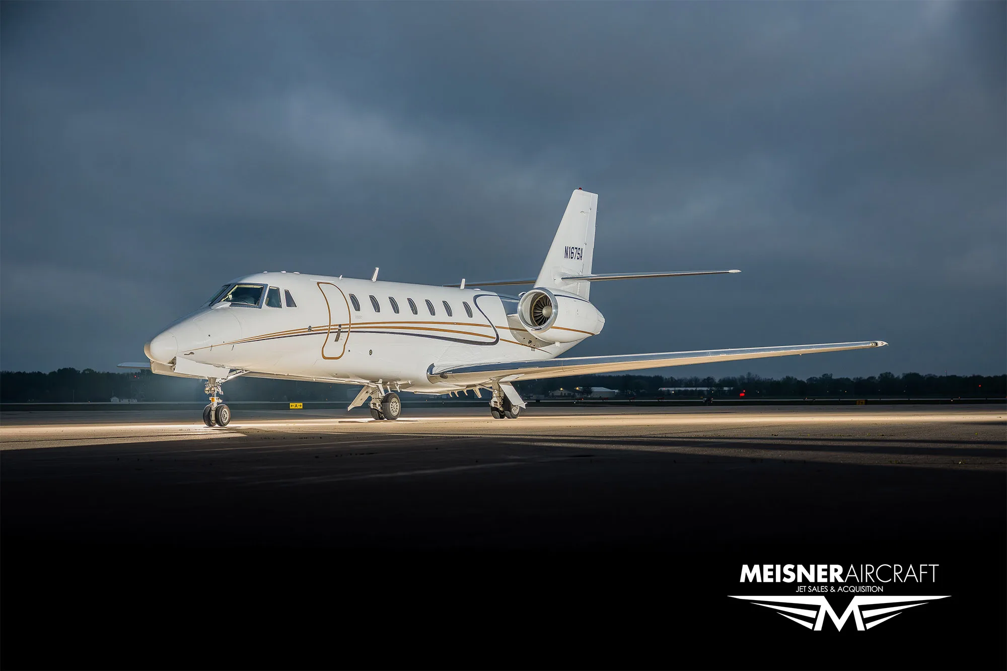 A white Cessna Citation business jet with tail number N167SA parked on an airfield at dusk, illuminated by ground lights.