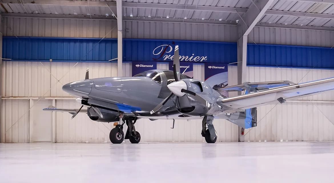 A low-angle front view of a gray and blue Diamond DA62 aircraft, registration N215E, in a hangar.