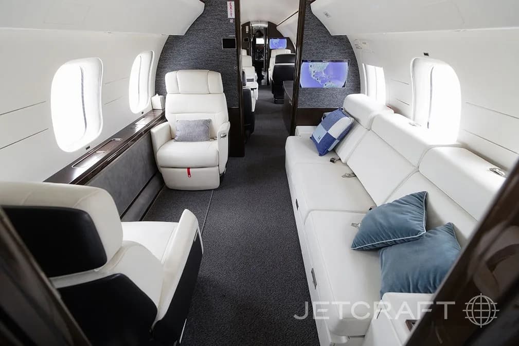 A private jet cabin with a long white sofa and a single white armchair, looking towards the rear.