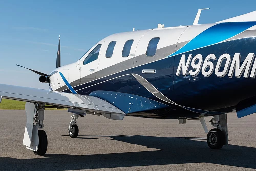 A close-up view of the fuselage and wing of the TBM 960 aircraft, showing registration N960MR and blue and white paint.