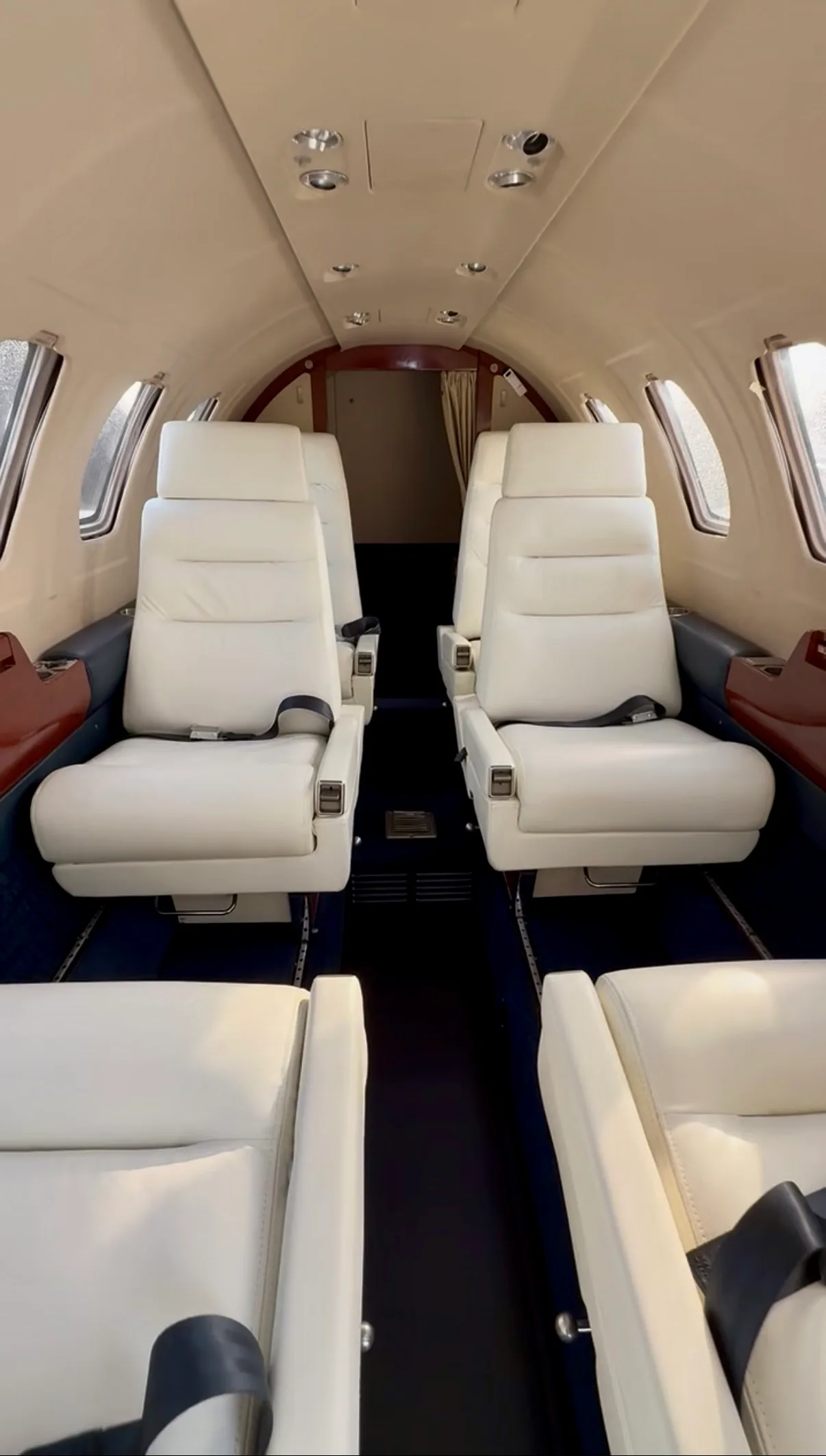View looking aft inside the aircraft cabin, showing rows of light-colored leather passenger seats.
