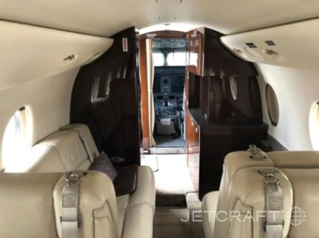 The aircraft's interior cabin looking forward, with cream seats and a view into the cockpit.