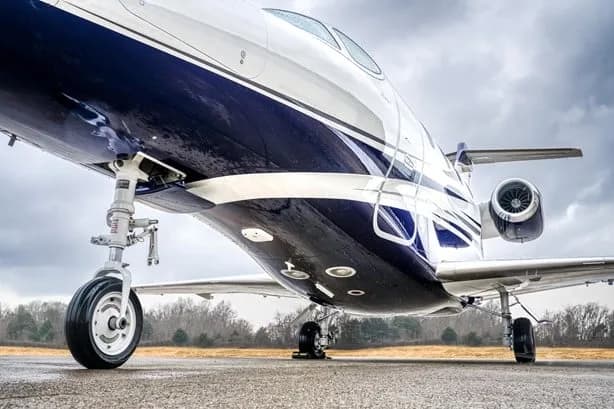 A low-angle view of the front landing gear and fuselage of a white and blue business jet.