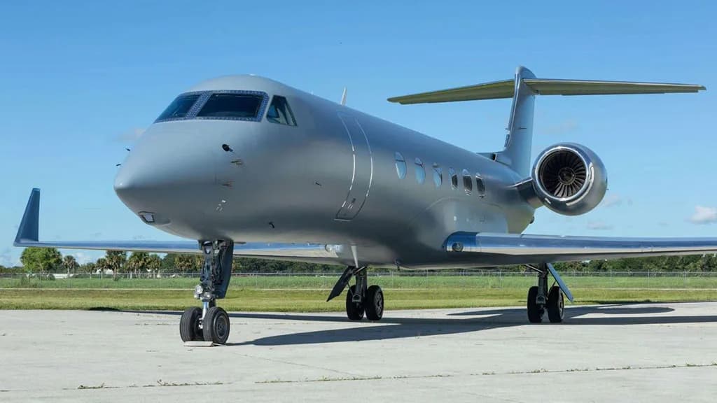 A grey Gulfstream G550 aircraft parked on a tarmac under a clear blue sky.