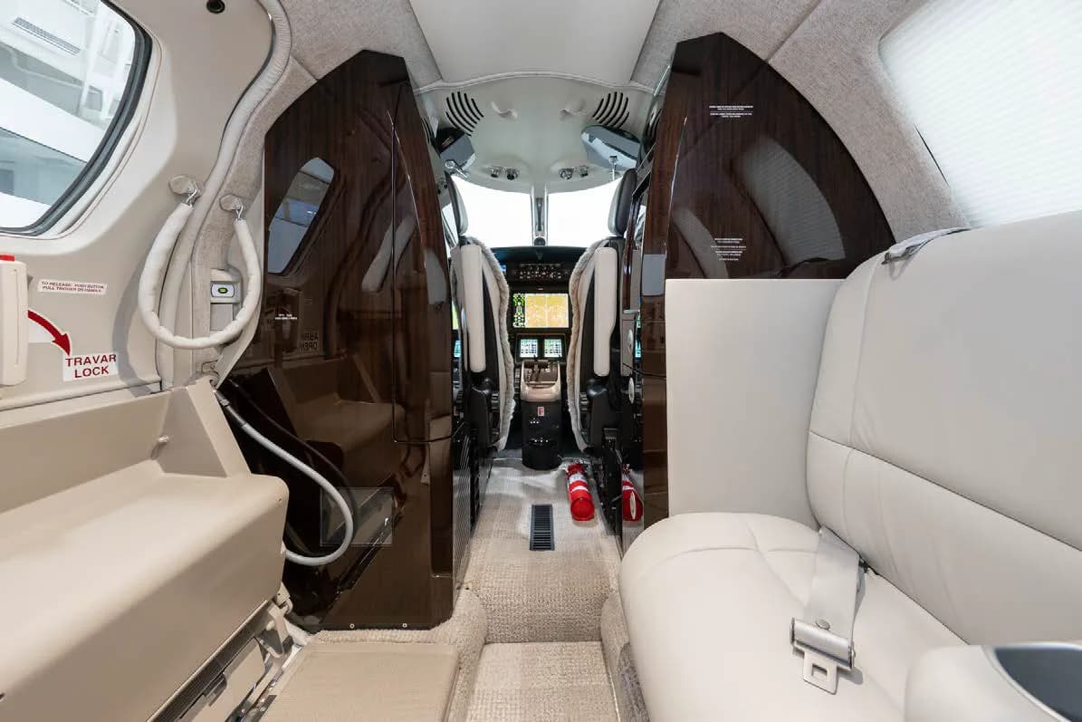 A view from the rear of the private jet cabin looking forward into the cockpit, showing dark wood accents and a fire extinguisher.