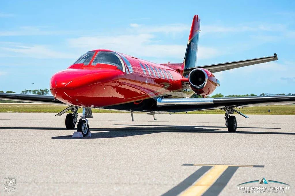 A three-quarter front view of the red and black Cessna Citation V jet on a tarmac.