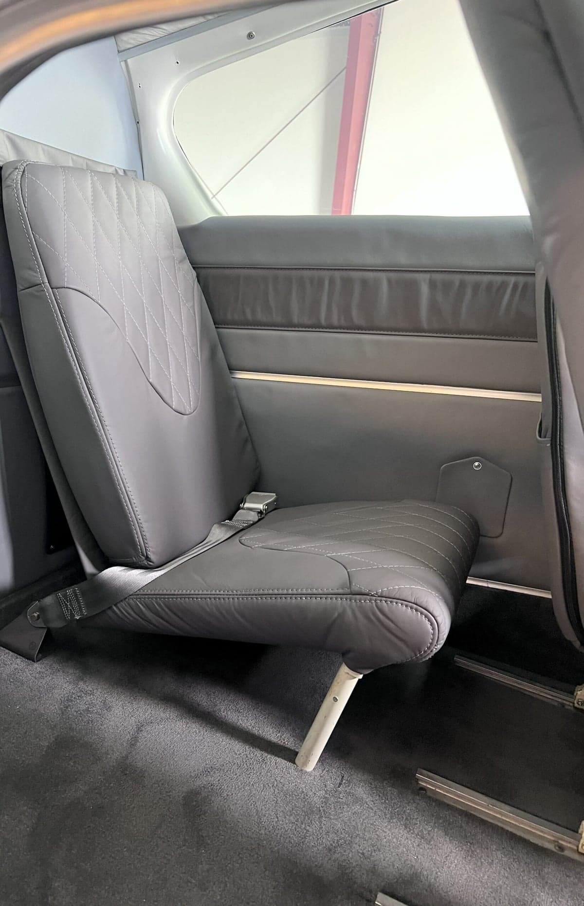 A single gray leather seat with diamond stitching is shown inside the aircraft's cabin.