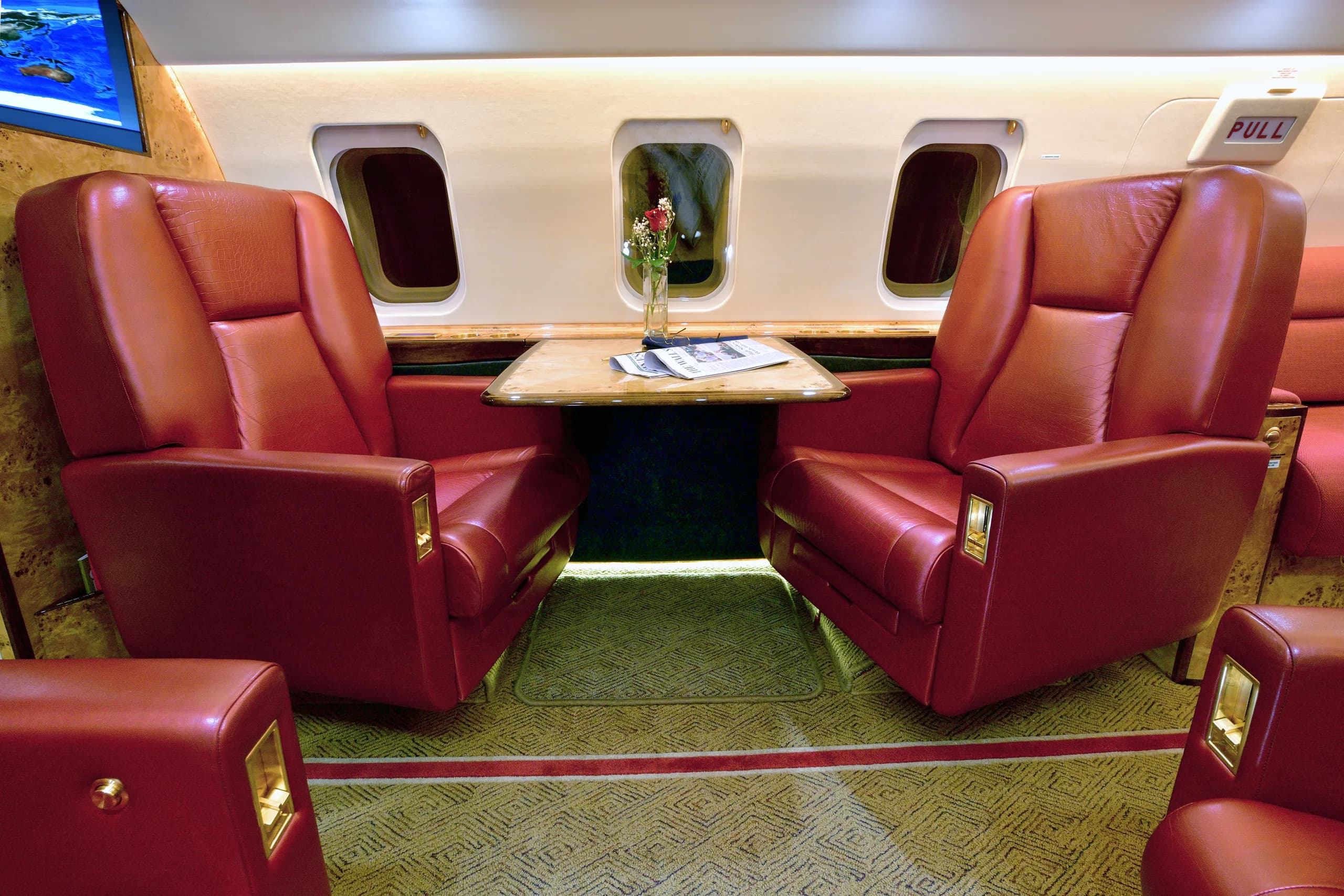 A close-up view of two red leather seats facing each other with a wooden table between them in a private jet cabin.