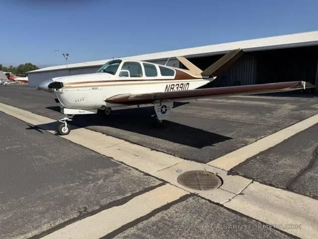 A white and brown Beechcraft Bonanza aircraft (N8391D) parked on an asphalt tarmac in front of a hangar.