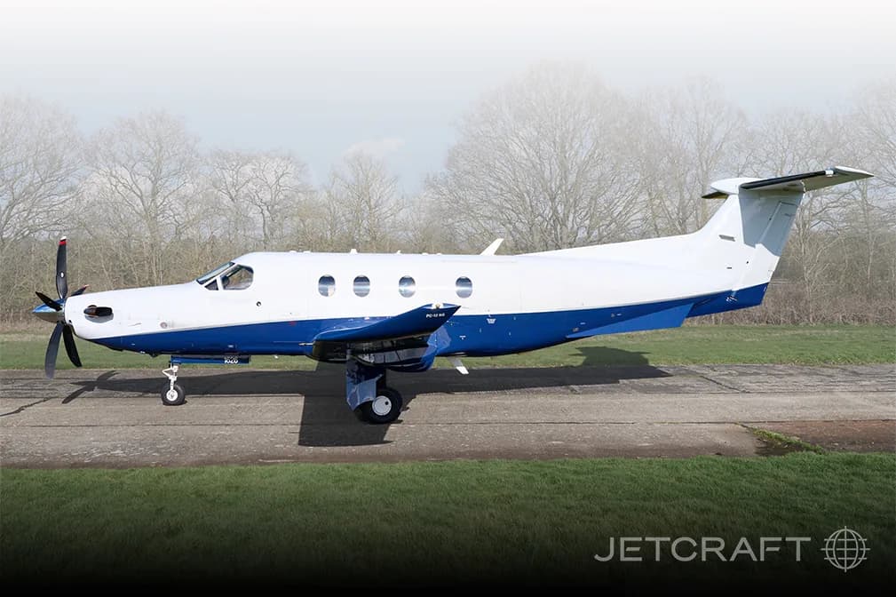 A white and blue Pilatus PC-12 is parked on the tarmac.