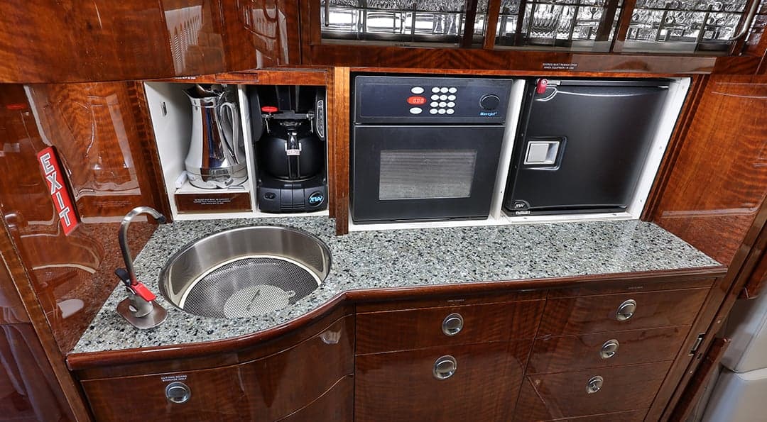 A galley area with wood cabinetry, a sink, and appliances.