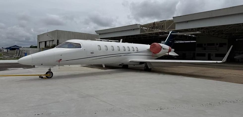 Side view of a white Learjet on the tarmac in front of a hangar.