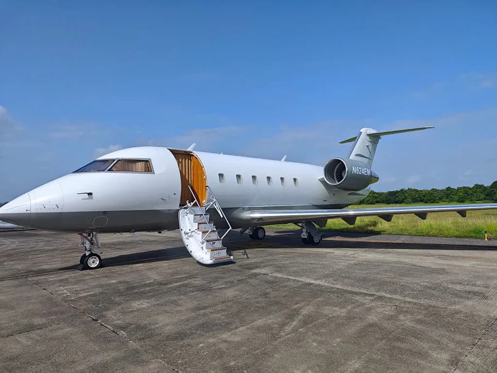 A white and grey Bombardier Challenger 604 business jet, N624EM, parked on an airfield with its main door open and stairs extended.