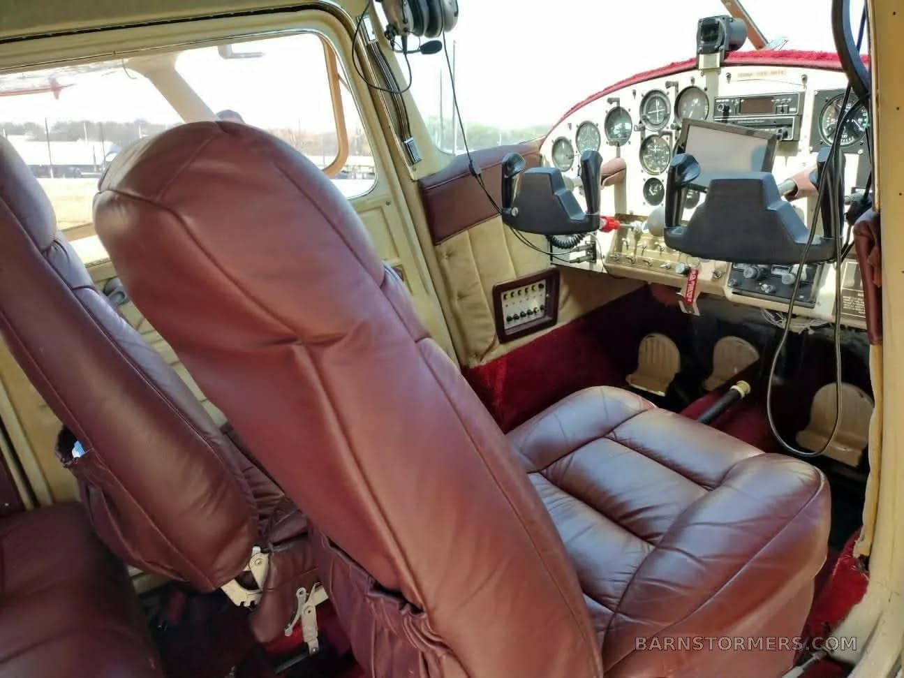 The interior of an aircraft cabin with two brown leather seats in the foreground and the instrument panel visible in the background.